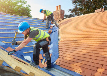 a roofer nails on the roof tiles